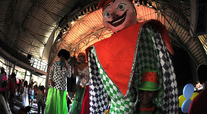 Bloco de carnaval no circo voador, com bonecos gigantes e pernas de pau animando a festa.